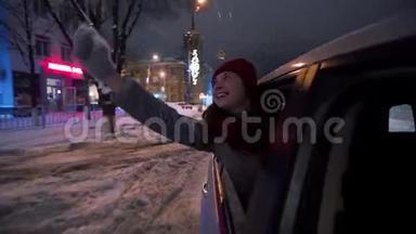 年轻快乐的女人站在<strong>车窗外</strong>，在下雪的冬夜玩着火花。 漂亮女孩开<strong>车</strong>很有趣